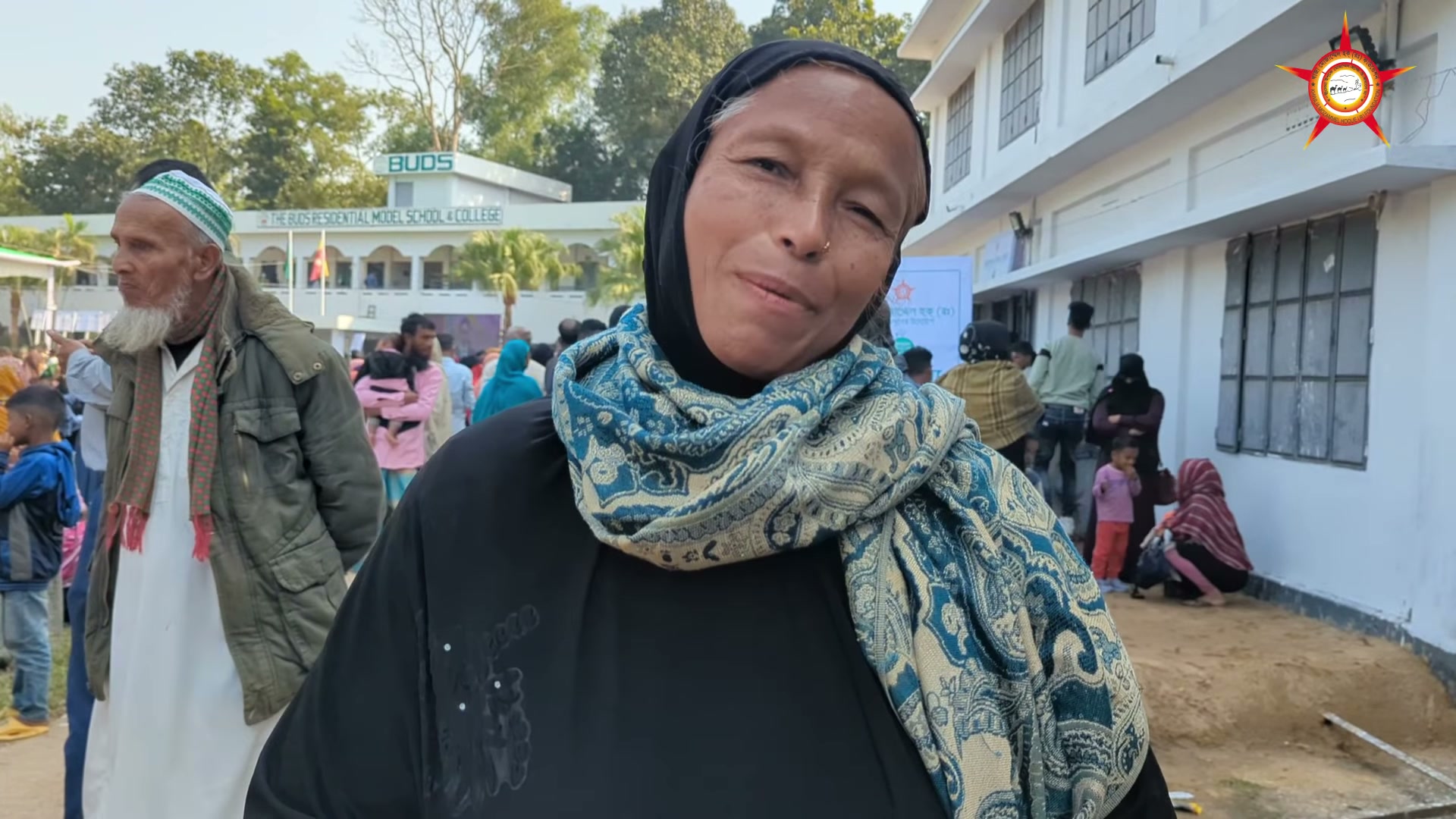 An attendee speaking to the camera at the 2024 medical camp, with the camp building behind.
