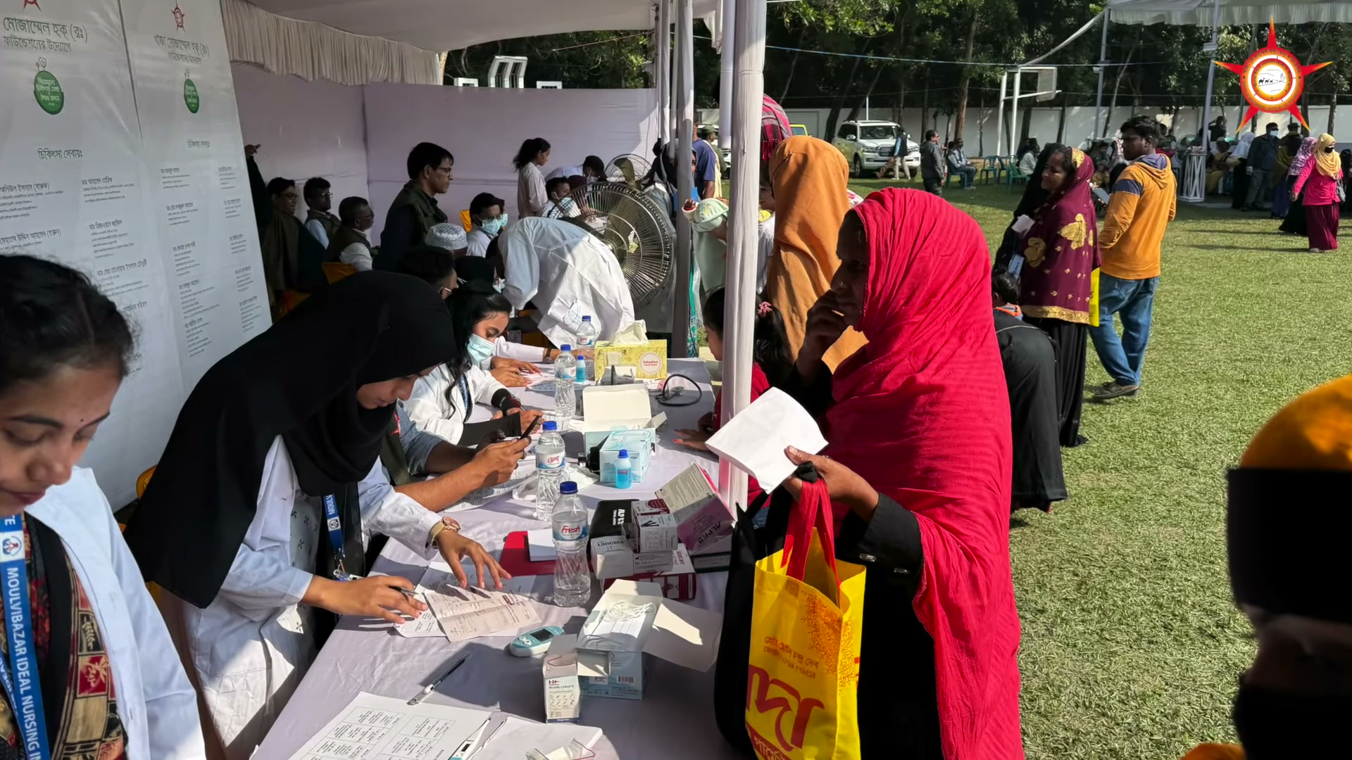People waiting beside tables during the medical camp.